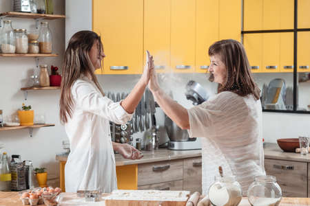Family teamwork. Leisure in kitchen. Pastry cooking. Amused mother and daughter giving high five. Well done.の写真素材
