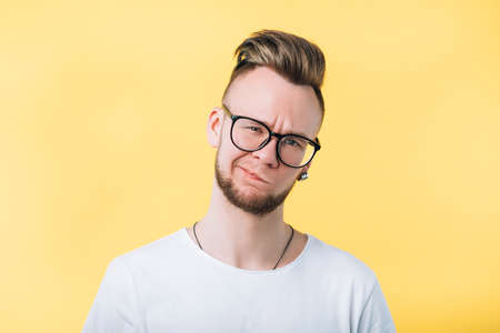 Portrait of sceptic hipster guy on yellow background. Young emotional man with comb over haircut....