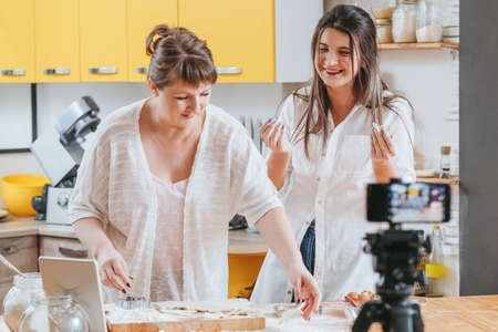 Family cooking blog. Two women mother daughter baking shooting video. Pastry dough on counter....