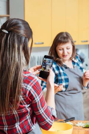 Healthy nutrition food blog business hobby. Mother daughter in kitchen cooking balanced meal taking smartphone picturesの写真素材