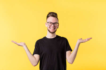 Portrait of cheerful millennial guy smiling, showing both hands open palms, comparing your options. Copy space.の写真素材