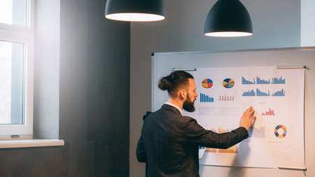 Business analyst studying company growth rates. Young man standing at the whiteboard with graphs. Copy space.の写真素材