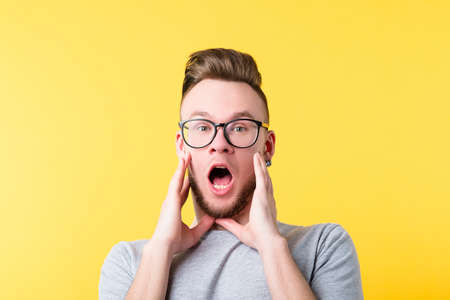Portrait of amazed hipster guy on yellow background. Young emotional man in glasses. Frightened facial expression. Copy space.の写真素材
