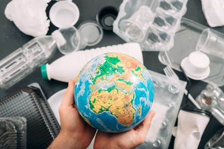 Earth drowned in plastic garbage. Closeup of globe in human hands. Ecology problem.の写真素材