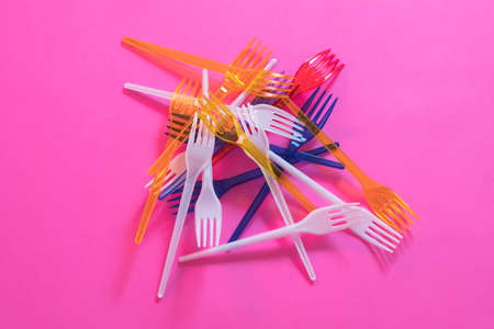 Plastic littering. Ecology problem. Multicolor disposable forks garbage dump over pink background.