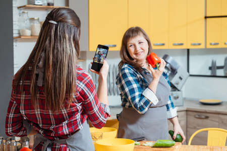 Family cooking blog. Women mother daughter taking photos with smartphone promoting healthy lifestyle diet eating habitの写真素材