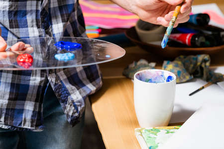 Artist at work. Paints on palette paintbrush in hand. Focus on creative idea. Artwork in process....