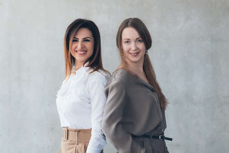 Young business ladies. Friends corporate colleagues back to back. Smiling confident smart successful company females.の写真素材