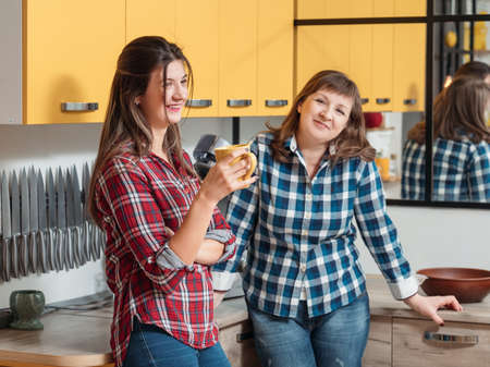 Family leisure. Quality time. Casual communication. Mother and adult daughter enjoying conversation in kitchen.の写真素材