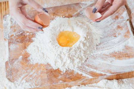 Homemade bakery food and pastry. Culinary course. Closeup of female hands cracked egg straight into flour.の写真素材