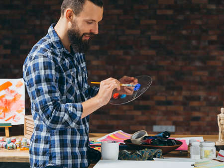 Art school workshop therapy. Smiling bearded painter mixing colors on palette. Creativity...