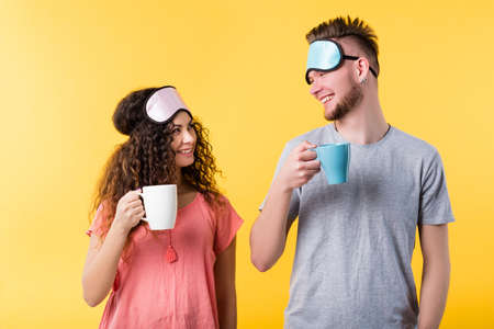 Lifestyle wake up habit. Healthy sleep good morning. Happy young couple smiling widely holding cups masks on foreheadの写真素材