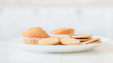 Homemade pastry. Sweet snacks. Closeup of plate with cookies and muffins on table in white kitchen....