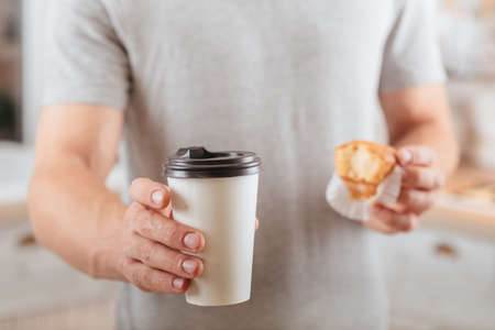 Coffee break. Take away. Man holding muffin and disposable mockup cup with hot drink.の写真素材
