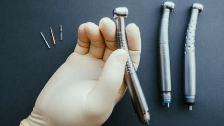 Professional tools. Hand of dentist in latex protective gloves holding dental drill handpiece.の写真素材