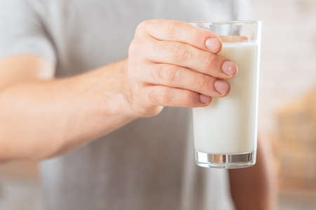 Dairy products. Balanced nutrition. Closeup of glass of soy milk in man hand. Blur background.の写真素材