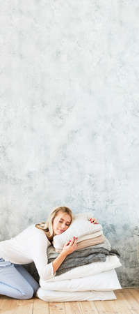 Natural home textile. Woman enjoying rest on pile of cozy pillows. Gray wall background. Copy space.