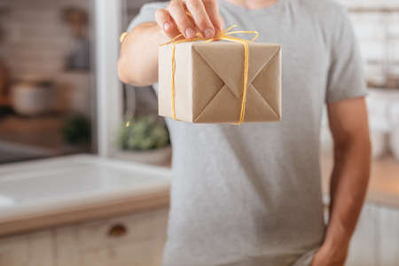 Special occasion. Cropped shot of man holding rustic paper handmade gift box. Blur kitchen background.の写真素材