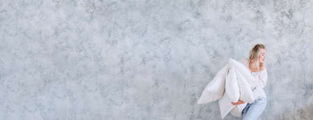 Home comfort. Happy lady running with feather pillow pile. Gray wall background. Copy space.