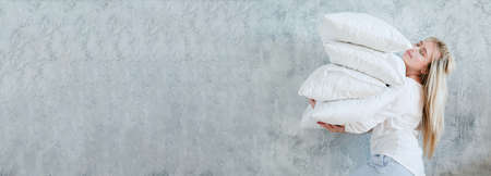 Happy housewife. Morning chores. Woman holding pile of pillows on gray background. Copy space.の写真素材