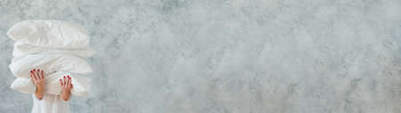 Natural home textile. Woman holding big pile of white soft pillows. Gray wall background. Copy space.の写真素材