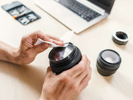 Photographing equipment care service. Cropped shot of technician cleaning camera lens with wet wipe.の写真素材