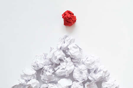 Social pyramid concept. Flat lay of crumpled same color paper balls under dominant individual red one. White background.の写真素材