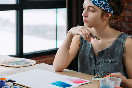 Creativity and imagination. Portrait of pensive female painter looking for inspiration. Blur window background.の写真素材