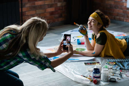 Creative art photo shooting. Lady posing on floor with paint and brush, smiling.の写真素材
