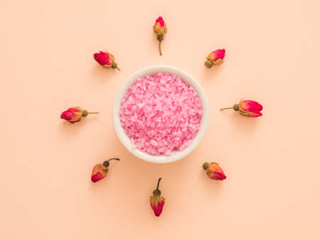 Organic body care products. Top view of rose buds around white bowl with pink bath salt. Peach background. Copy space.の写真素材