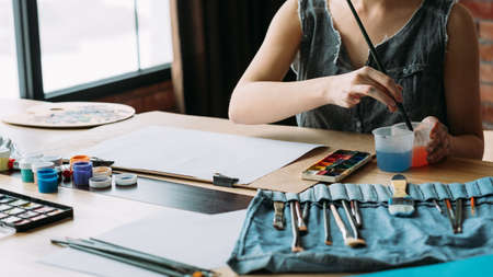 Creative occupation. Cropped shot of female artist using watercolor for painting, washing brush.の写真素材