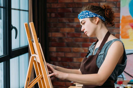 Talent and skills. Side view of creative female artist using easel for painting abstract artworks.