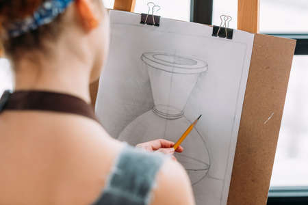 Art studio. Closeup back view of lefthanded painter measuring proportions with pencil in drawing vase.の写真素材