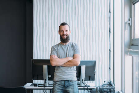 IT administration. Portrait of successful software engineer standing at workplace with arms folded, smiling. Copy space.の写真素材