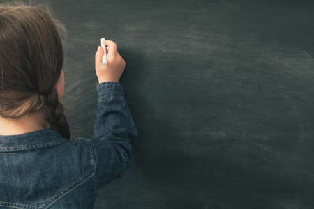 School and education. Back view of young girl writing on blank chalkboard. Copy space.