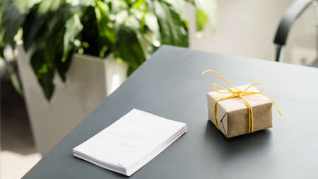 Boss special day. Wrapped gift box and blank paper stack on office desk. Blurred green plant in background. Copy space.の写真素材