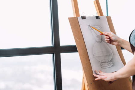 Art studio. Cropped shot of lady measuring proportions with pencil in drawing vase. Window background. Copy space.の写真素材