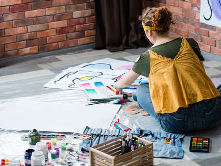 Art therapy. Back view of lady sitting on floor, painting abstract artworks with watercolor. Copy space.の写真素材