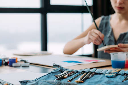Artist workplace. Closeup of paintbrush organizer. Inspired female painter working in studio. Blur background. Copy space.の写真素材