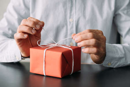 Corporate birthday party. Cropped shot of business man in shirt untying red gift box.の写真素材