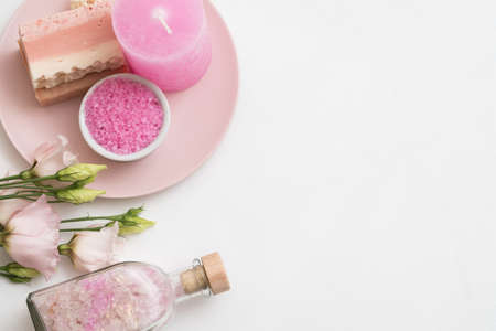 Spa aroma therapy. Flat lay of pink bath salt, handmade soap, candle and roses on plate. White background. Copy space.