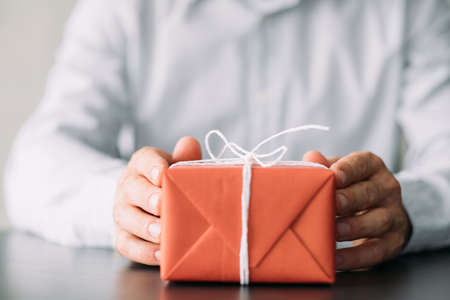 Office delivery service. Cropped shot of business man in shirt sitting at desk with red gift box....