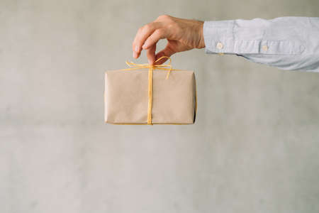 Office food delivery service. Cropped shot of business man holding paper wrapped box over gray wall background. Copy space.の写真素材