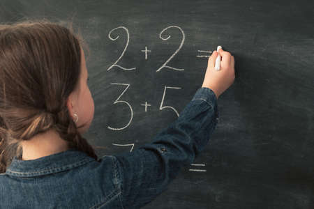 Primary school education. Back view of young girl doing math on chalkboard. Copy space.