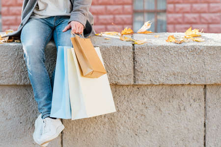 Shopaholic lifestyle. Cropped shot of man in casual outfit sitting on wall with packages. Fall urban background. Copy space.の写真素材