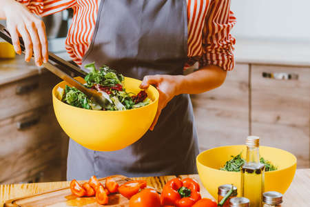 Vegetarian lifestyle. Cropped shot of woman cooking, mixing salad with fresh organic ingredients in yellow bowl.の写真素材