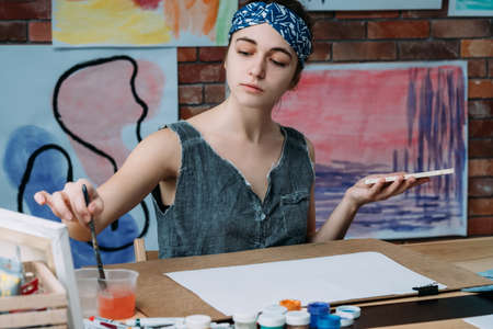 Contemporary artwork artist. Young lady painting in modern workshop, washing paintbrush.の写真素材