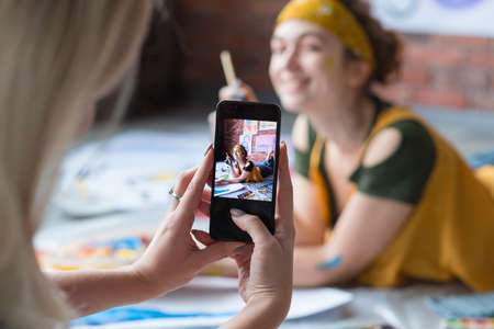Creative art photo shooting. Lady posing on floor with paint and brush, smiling. Blur background.の写真素材