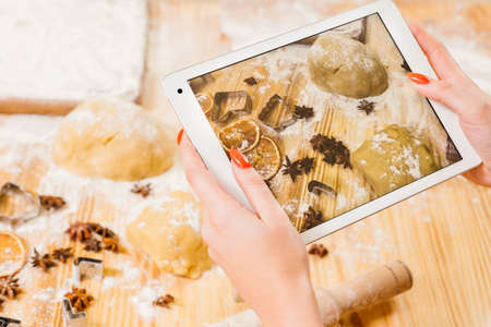 Electronic cookery book. Lady using tablet to take picture of chef workplace. Biscuit ingredients on...