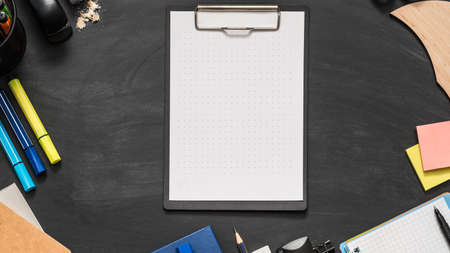 School supplies. Flat lay of marked white mockup sheet of paper on clipboard, stationery over black...